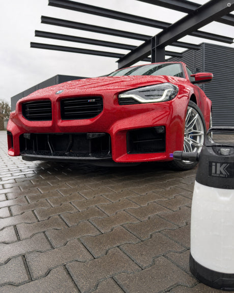 Die frisch gewaschene Front eines roten BMW mit runden Wassertropfen, vorn angeschnitten der iK Foam Pro 2 auf dem Pflaster.