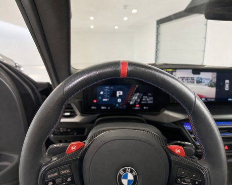 Speckig glänzendes Lederlenkrad eines weißen BMW M2 im Cockpit, der Fettglanz an der Zehn-Uhr-Position hebt sich von der matten Narbung ab — gezeigt im Artikel „Lederlenkrad reinigen: warum speckiger Glanz zwei Ursachen hat“