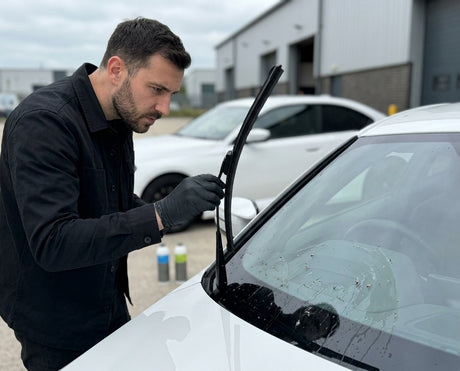 Detailing1 Daniel hebt den Scheibenwischer des weissen BMW M2 an und prueft die verschmierte Frontscheibe