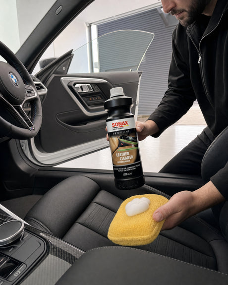 SONAX Profiline Leather Cleaner und ein Schaum-Pad in Daniels Hand am Ledersitz des weißen BMW M2.