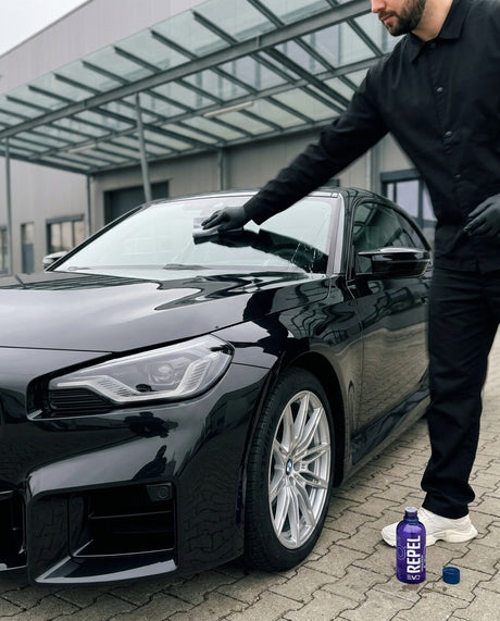 Daniel trägt GYEON Q² View EVO Rain Repellent Glasversiegelung mit dem Applikator-Pad auf die Windschutzscheibe eines schwarz